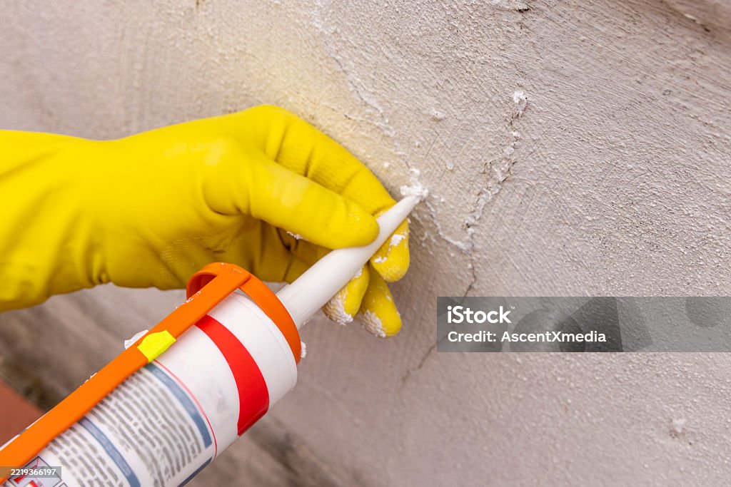 Restoration detail of man's hands filling crack in outdoor wall with silicone, liguria